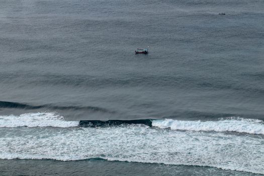 Aerial view of Nyang Nyang beach on Bali in Indonesia. A popular spot of surfers with big waves in the Indian Ocean. Fishing boats of Balinese fishermen on the sea surface. Waves break off the coast.