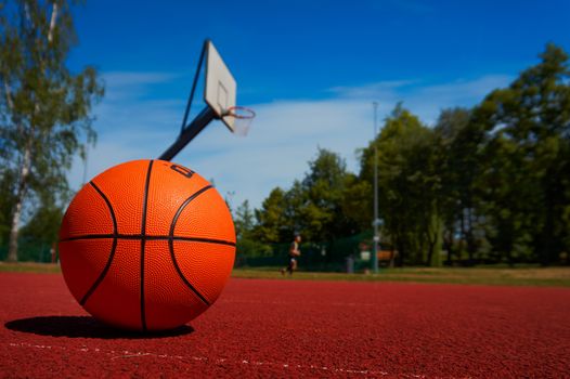 Basketball on outdoor basketball court floor against the trees and blue cloudy sky. Free copy space.