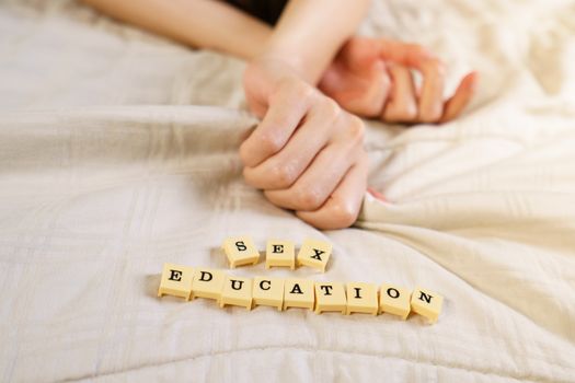 Woman hand sign orgasm on bed with scrabble board showing words sex education.