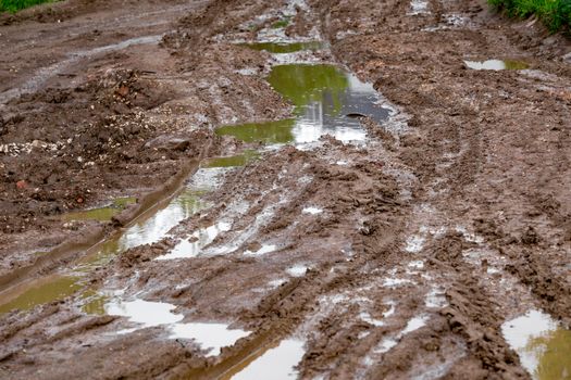 dirty clay mud crossroads with puddles and tire tracks - close-up with selective focus and linear perspective.
