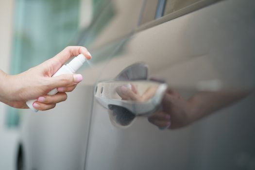Hand hold bottle alcohol spraying disinfecting door handle of car, for corona virus or Covid-19 protection.