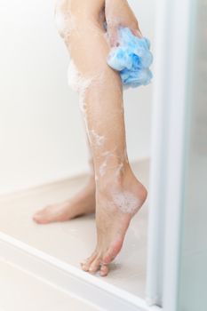 Woman washing her leg with bath sponge.