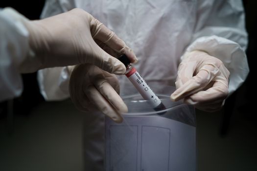 Doctor in a protective suit. taking blood test sample tubes with COVID-19 from a plastic zipper bag in laboratory.(Blood) (Fake QR code and barcode)