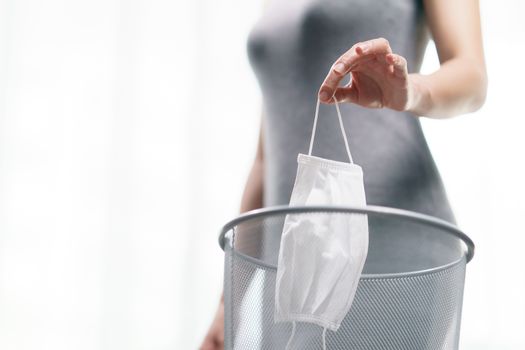 Woman dumped a used medical face mask into the trash, corona virus or Covid-19 protection.