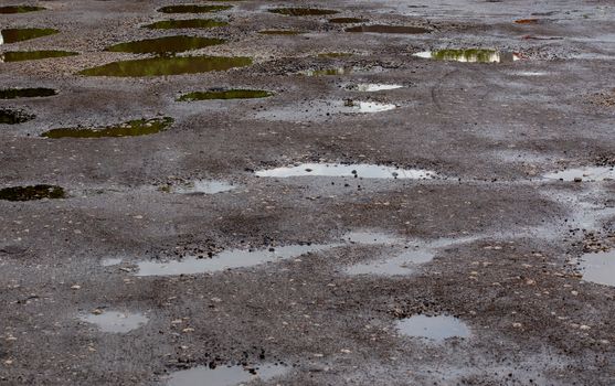 bumpy damaged road asphalt with multiple puddles after rain at summer daytime, potholes.