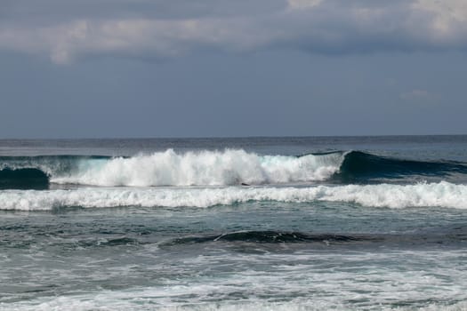 Young caucasian man surfs the ocean wave and makes a lot of splashes into the camera. Nyang Nyang Surf Spot in Bali, Indonesia. The surfer falls into the ocean waves. Man rides the wave at sunny day.