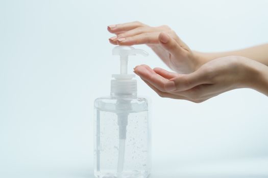 Hand with hand sanitizer in a clear pump bottle on a white background.