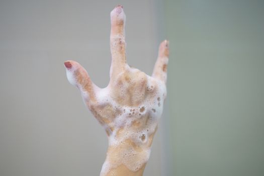 Hand with soft foam bubble from soap is showing I Love You language hand sign.