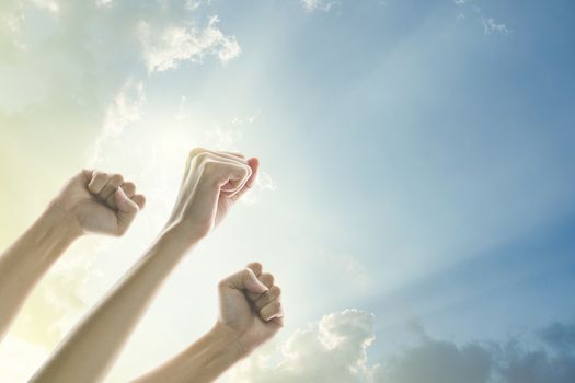 Fists of people raised in the air with clear sky and sunlight background.