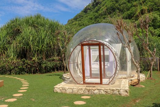 Romantic bubble hotel with transparent walls. White wooden double bed with mosquito net inside bubble house. Honeymoon in an inflatable tent. Tourist attraction in tropical paradise on Bali, Indonesia