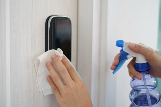 Woman hand using napkin and detergent spray cleaning doorknob for corona virus or Covid-19 protection.