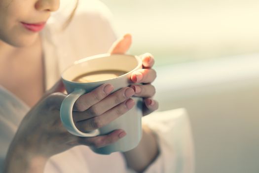 Woman hands holding hot cup of coffee or tea in morning sunlight.