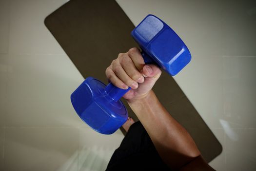 Man hand holding blue dumbbell above
yoga mat.