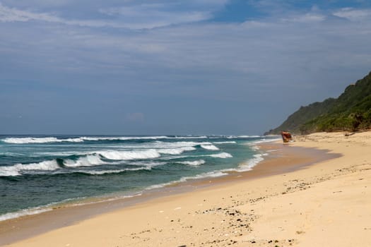 Virgin beach with fine yellow sand on Bali island. Tropical paradise with Nyang Nyang beach with high cliff on background. Wild waves are approaching the shore in rows. Sea foam in rolling waves.