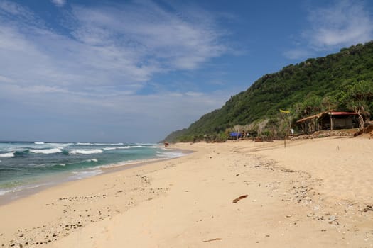 Virgin beach with fine yellow sand on Bali island. Tropical paradise with Nyang Nyang beach with high cliff on background. Wild waves are approaching the shore in rows. Sea foam in rolling waves.