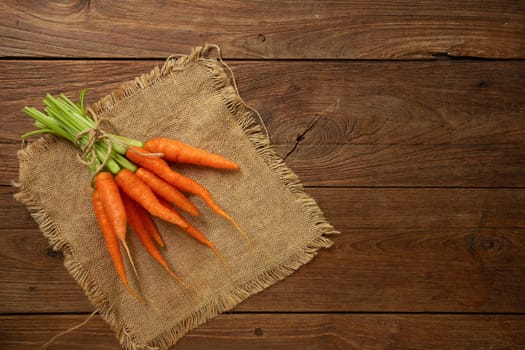 Fresh baby carrots on wooden cutting board and wooden background.