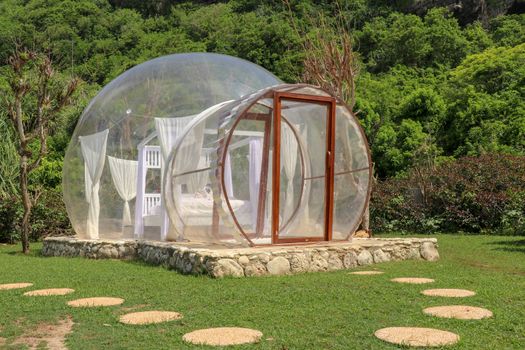 Romantic bubble hotel with transparent walls. White wooden double bed with mosquito net inside bubble house. Honeymoon in an inflatable tent. Tourist attraction in tropical paradise on Bali, Indonesia