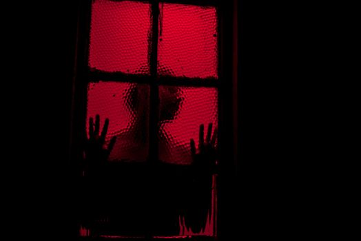 Person leaning against window in room filled with red light
