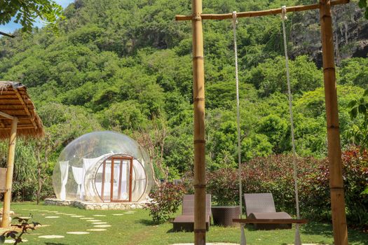 Romantic bubble house with transparent walls. White wooden double bed with mosquito net inside bubble. Honeymoon in an inflatable tent. Tourist attraction in tropical paradise on Bali, Indonesia