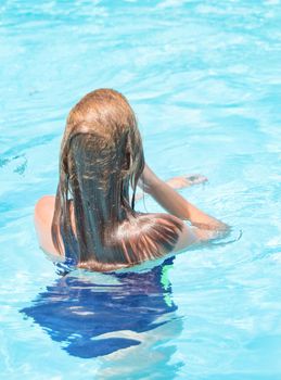 Happy girl with wet hair standing in the water in an outdoor pool, having fun in the water on vacation, vertical photo, back view.