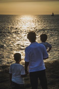 Father with children facing the sea at sunset
