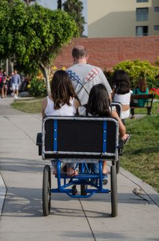 A man and four children on a three-seat bicycle in the park