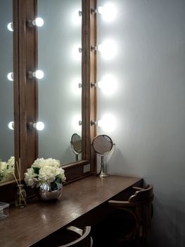 Makeup room classic and vintage style decoration with long wooden table, wooden chairs, mirrors with light bulbs and modern flower pot, vertical style.