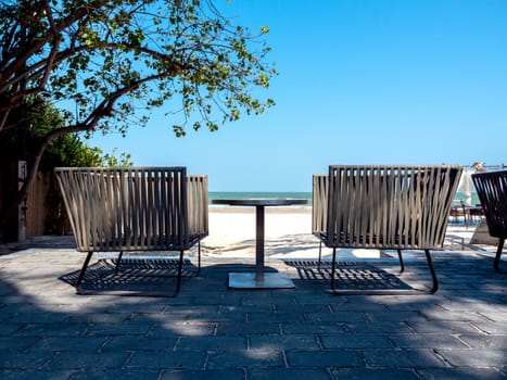 Modern chairs with round side table on balcony with sea view near the beach on blue sky background.