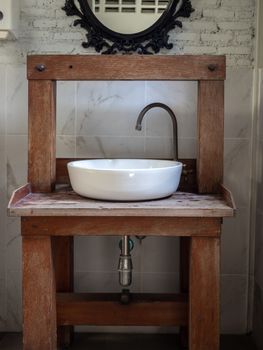 White clean ceramic sink bath and faucet on vintage wooden table and vintage mirror on white brick wall background vertical style.