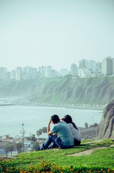 A couple sitting on the edge of the cliff on the coast of Lima - Peru facing the sea