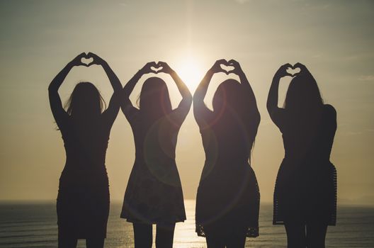 Girls in front of the sunset raising their hands forming a heart