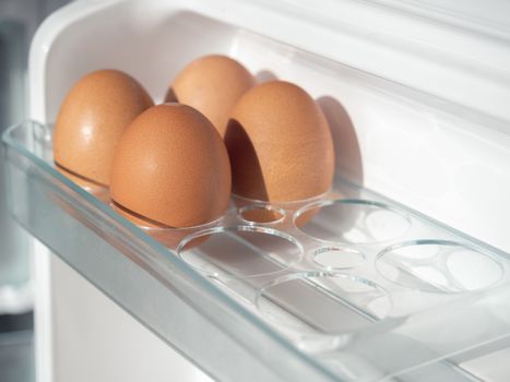 Four fresh chicken eggs on shelf of white refrigerator.