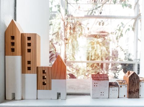 Miniature wooden houses on white shelf near window glass with sunlight, Stay safe stay at home concept.