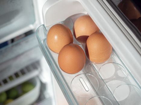 Four fresh chicken eggs on shelf of white refrigerator, top view.