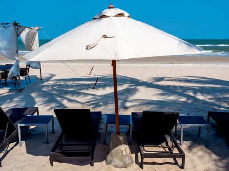 Empty wooden sunbed and beach umbrella on sand beach with sea view on blue sky background.