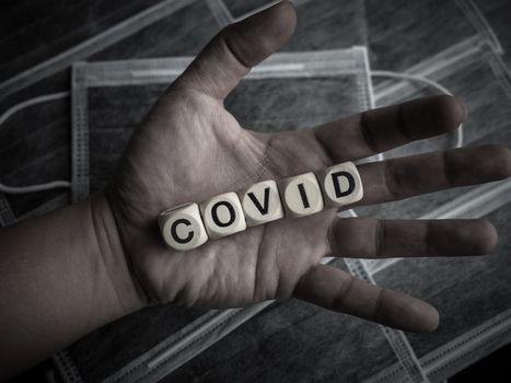 Coronavirus or Covid-19 concept. Wooden cubes text "COVID" in hand on protective face mask background.