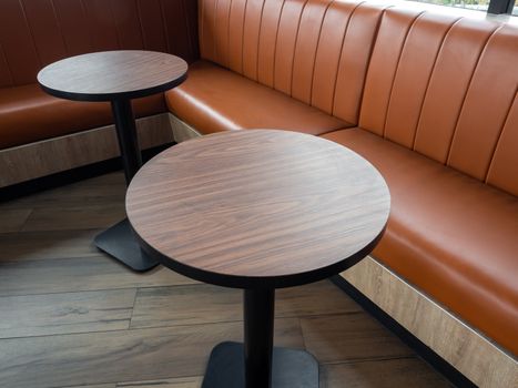 Furniture decoration in cafe retro style. Empty round wood table bars and orange long leather sofa on wood floor with natural daylight.