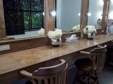 Makeup room classic and vintage style decoration with long wooden table, wooden chairs, mirrors with light bulbs and modern flower pot.