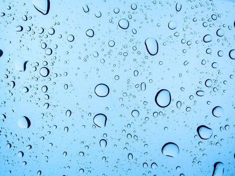 Water droplet on glass background. Light blue water drops texture on windshield on rainy day.