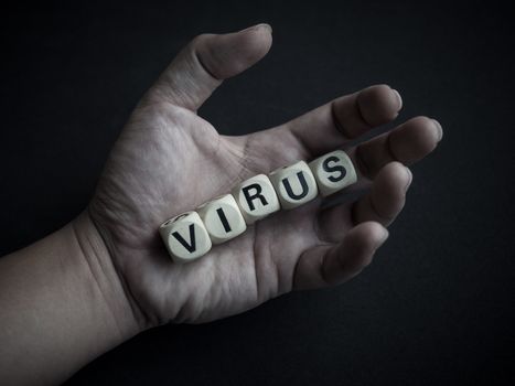 Coronavirus or Covid-19 concept. Wooden cubes text "VIRUS" in hand on dark background.