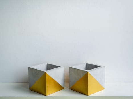 Cactus pot. Concrete pot. Two empty modern geometric concrete planters with gold painted on white wooden shelf isolated on white wall background.