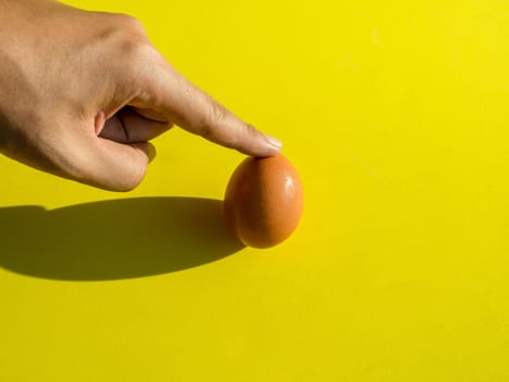 Finger touching or pointing fresh chicken egg isolated on yellow background, minimalist trendy style.