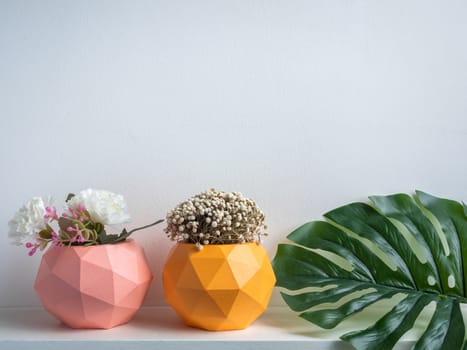 Cactus pot. Concrete pot. Pink and orange modern geometric concrete planters with flower and green palm leaf on white wooden shelf isolated on white background.