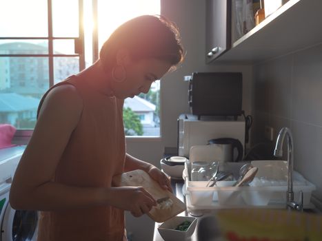 Beautiful Asian woman short hair chopped the spring onion on a wooden cutting board near the window in room in condominium in the evening. Cooking at home.