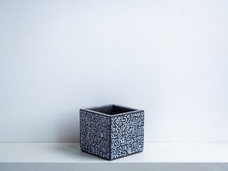 Cactus pot. Concrete pot. Empty black with modern graphic pattern geometric concrete planter on white wooden shelf isolated on white wall background.