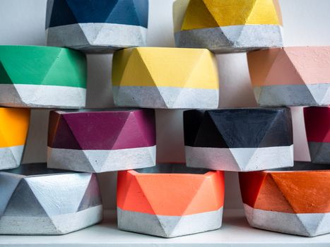 Cactus pot. Concrete pot. Close-up pile of empty colorful pentagon concrete planters on white wooden shelf isolated on white background.