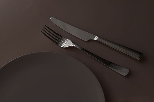 Empty plate and cutlery as mockup set on dark brown background, top tableware for chef table decor and menu branding design