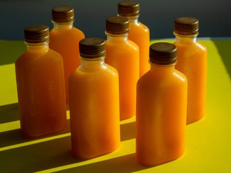 Orange juice iced cold in the bottles. Close-up square shape bottle with cold orange juice on yellow background minimalist style.