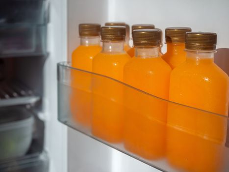 Orange juice iced cold in the bottles on shelf in refrigerator. Square shape bottle with cold orange juice.