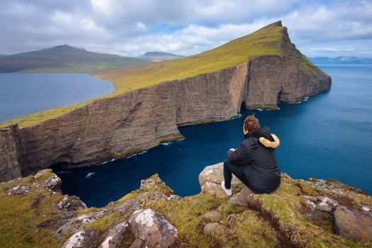 Hiker sitting on the edge of the cliff Traelanipan and looking at the lake Sorvagsvatn located on the island of Vagar. Leitisvatn or Sorvagsvatn is the largest lake in the Faroe Islands, Denmark.